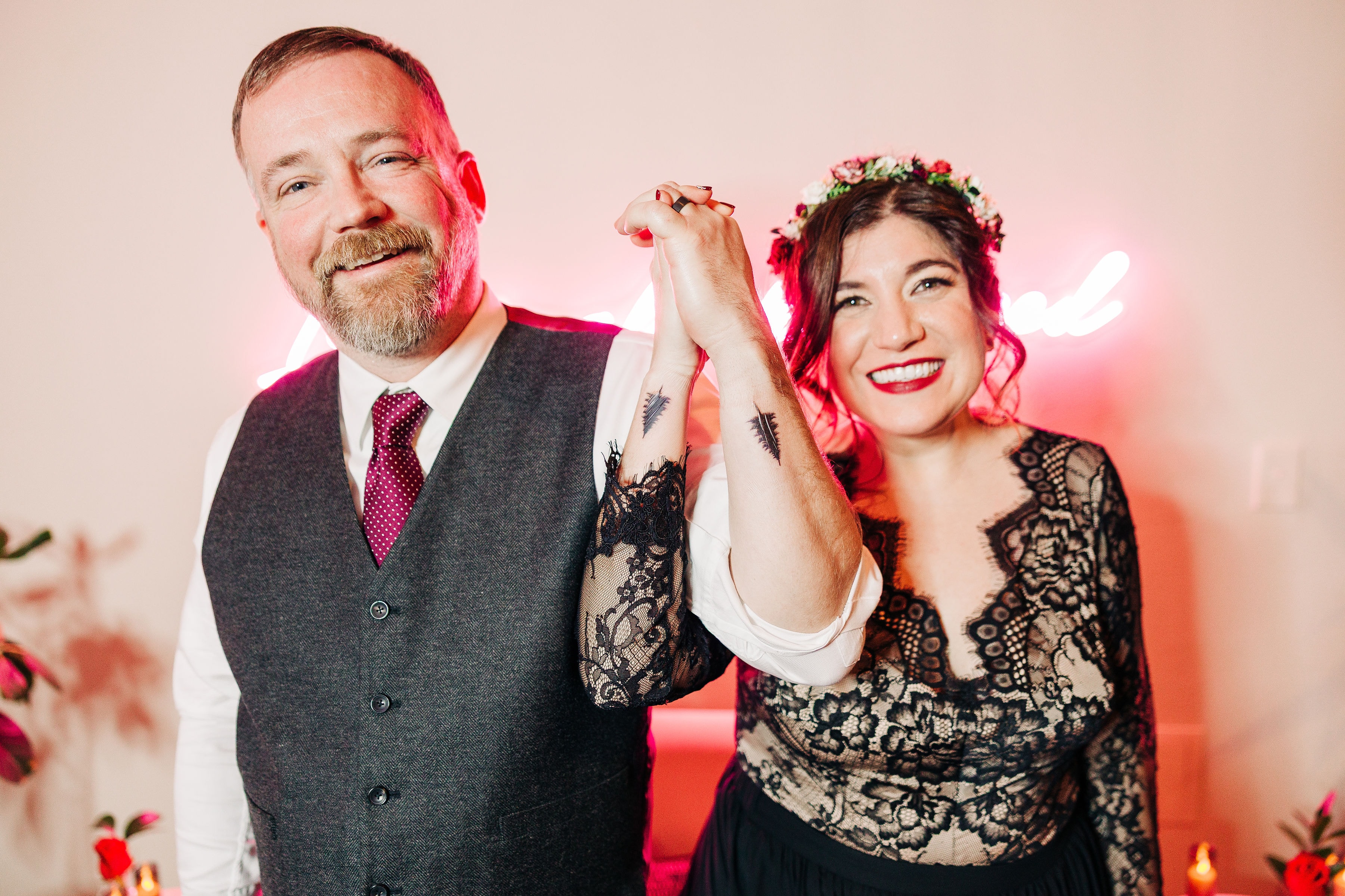 Billy & Jenn showing off their new matching tattoos of the silouette of a tall tree, done on their wrists. Both are smiling and looking at the camera while holding hands with the tattoos on their wrists.