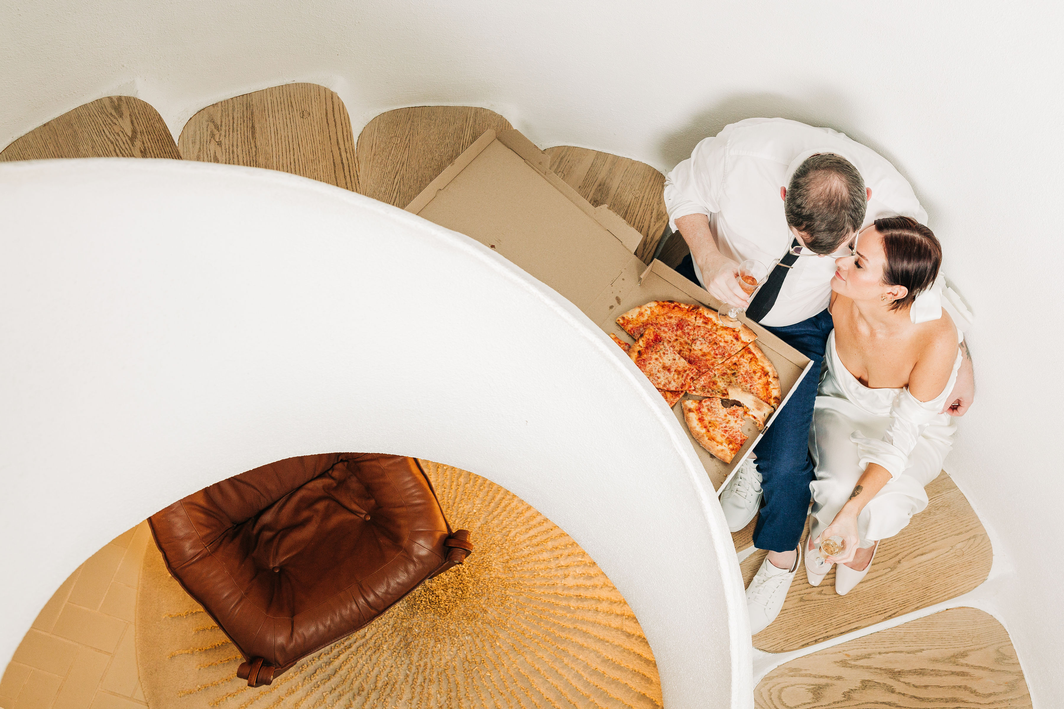 A couple sits on the stairs of the Airb&b sharing an intimate moment eating a pizza together, relaxed and in each others arms.