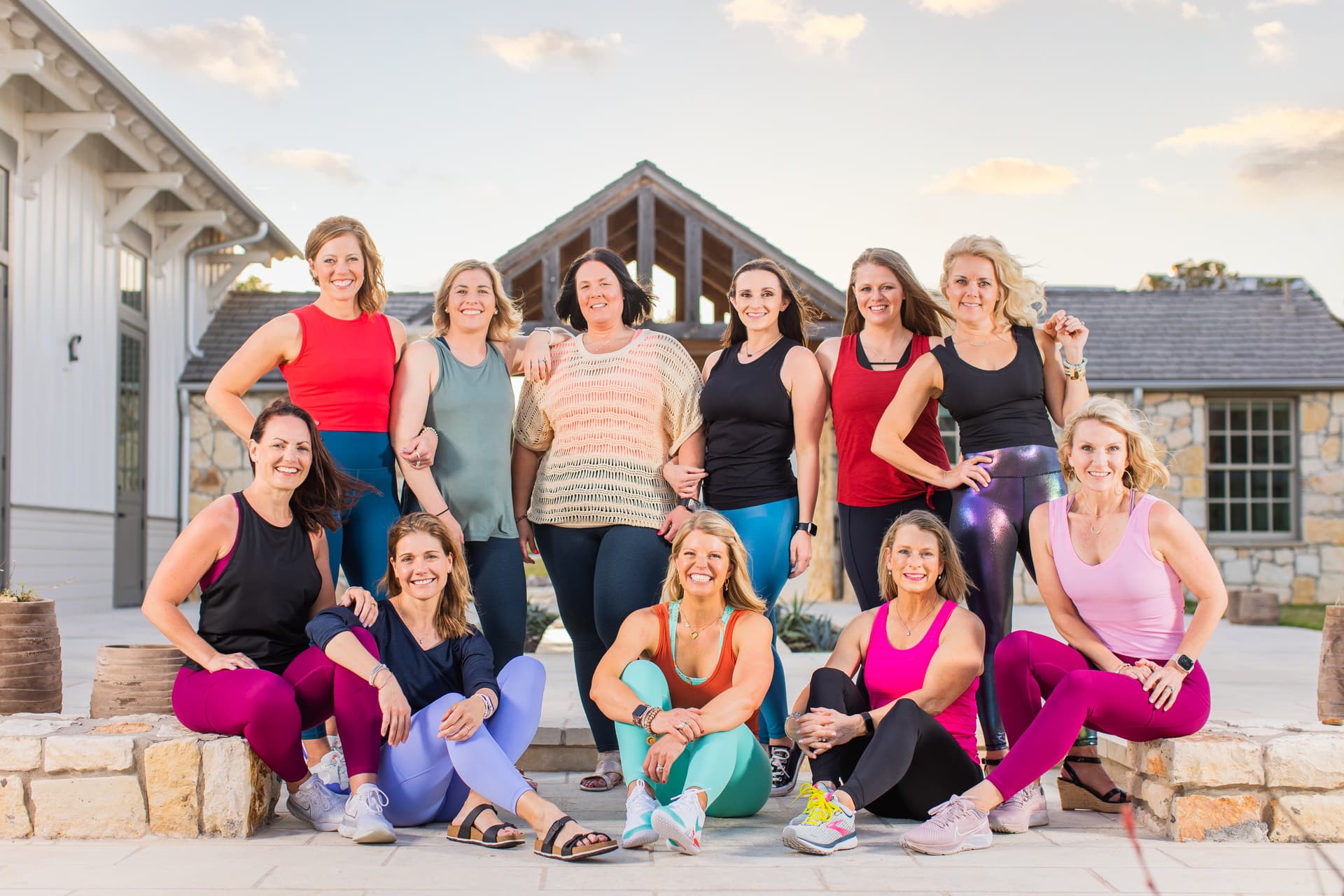 A warm group portrait of confident women in activewear. each is casual and relaxed, with arms around eachother and a joyful, fun loving expression. they wear colorful clothing, and have a warm glow of light surrounding them.