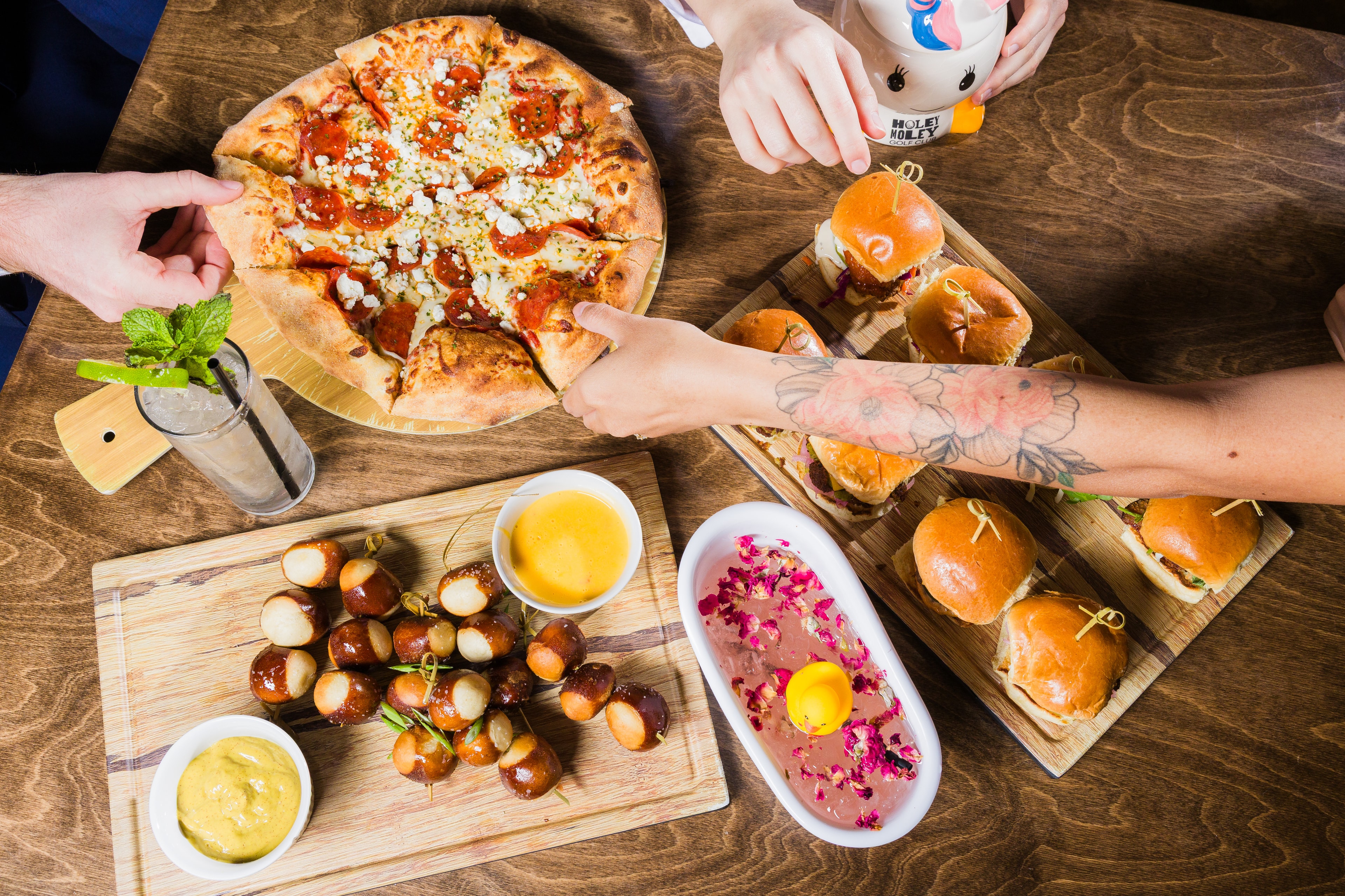 a close up of detail shots taken within a branding photoshoot, photos of the food offerings at the venue with hands reaching in to grab slices of pizza, drinks. lighting is vibrant and colorful.
