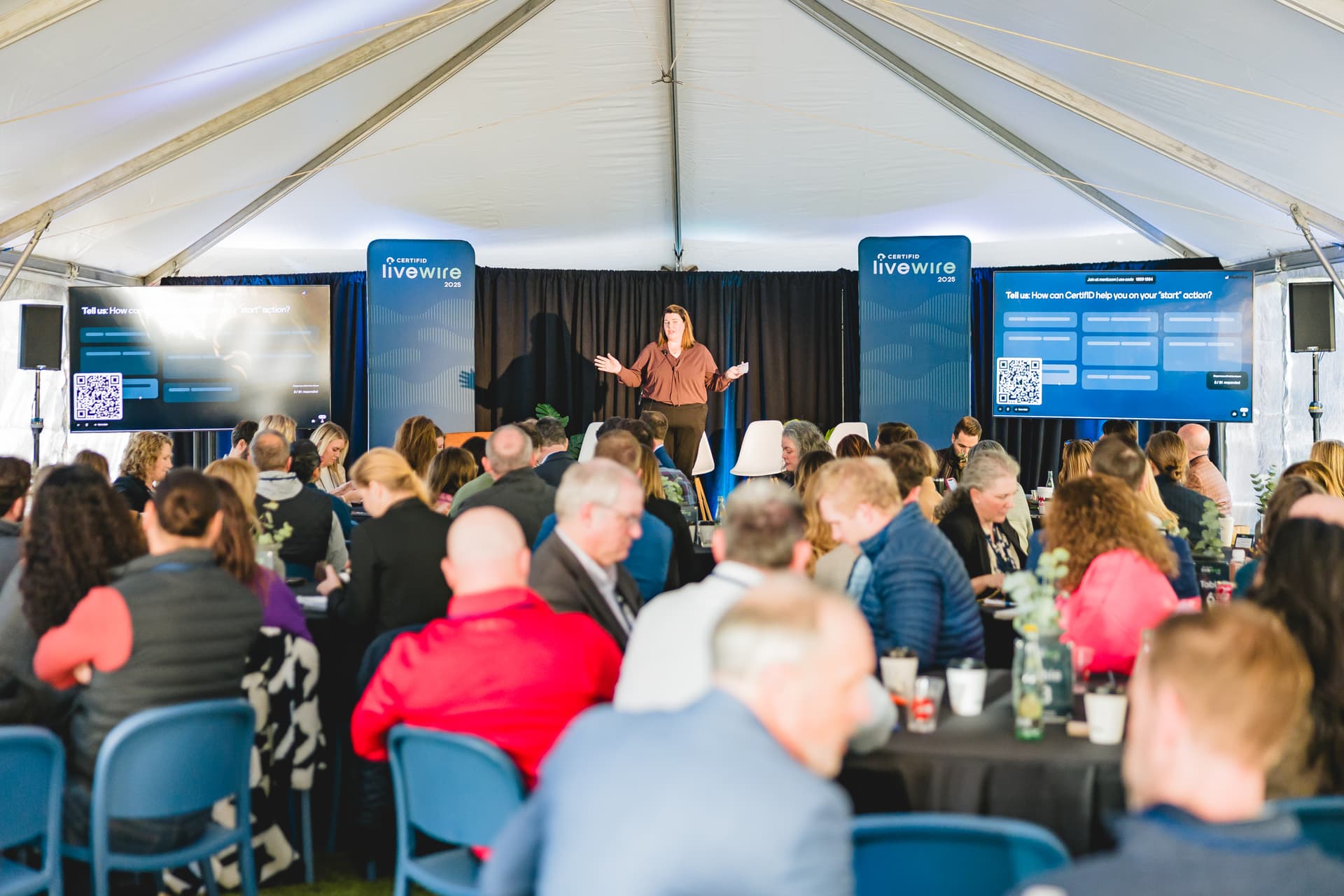 Keynote speaker on stage mid-presentation with an engaged audience visible in the foreground, warm natural lighting