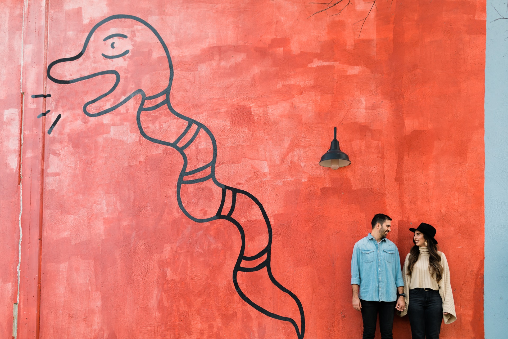 Couple holding hands and looking at eachother against a large colorful mural of Canopy Complex in East Austin, with warm natural light streaming in