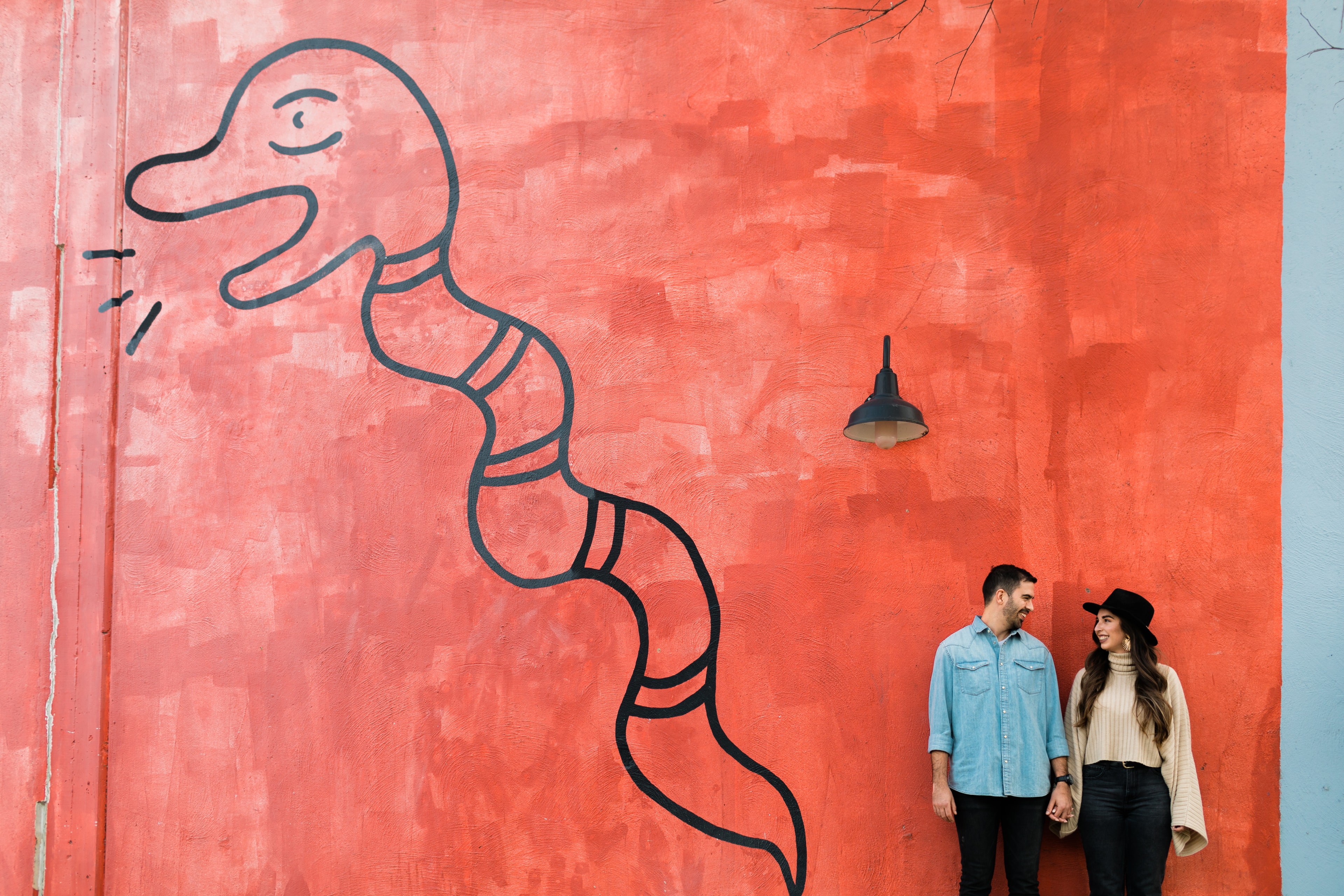 Couple holding hands and looking at eachother against a large colorful mural of Canopy Complex in East Austin, with warm natural light streaming in