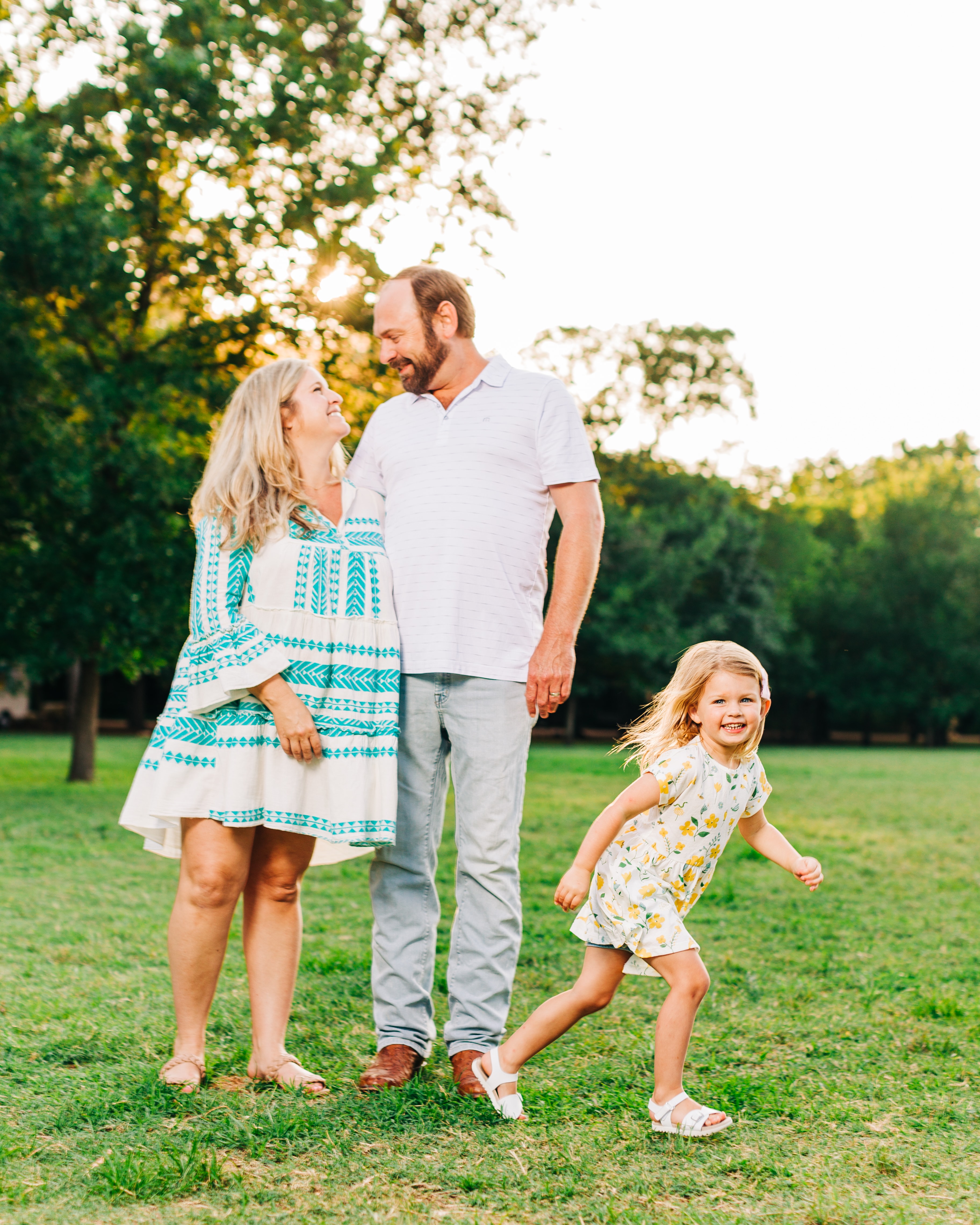 Family of three in coordinated pastel outfits — parents in blue, kids in textured white — cohesive but not matching, looking relaxed and natural together
