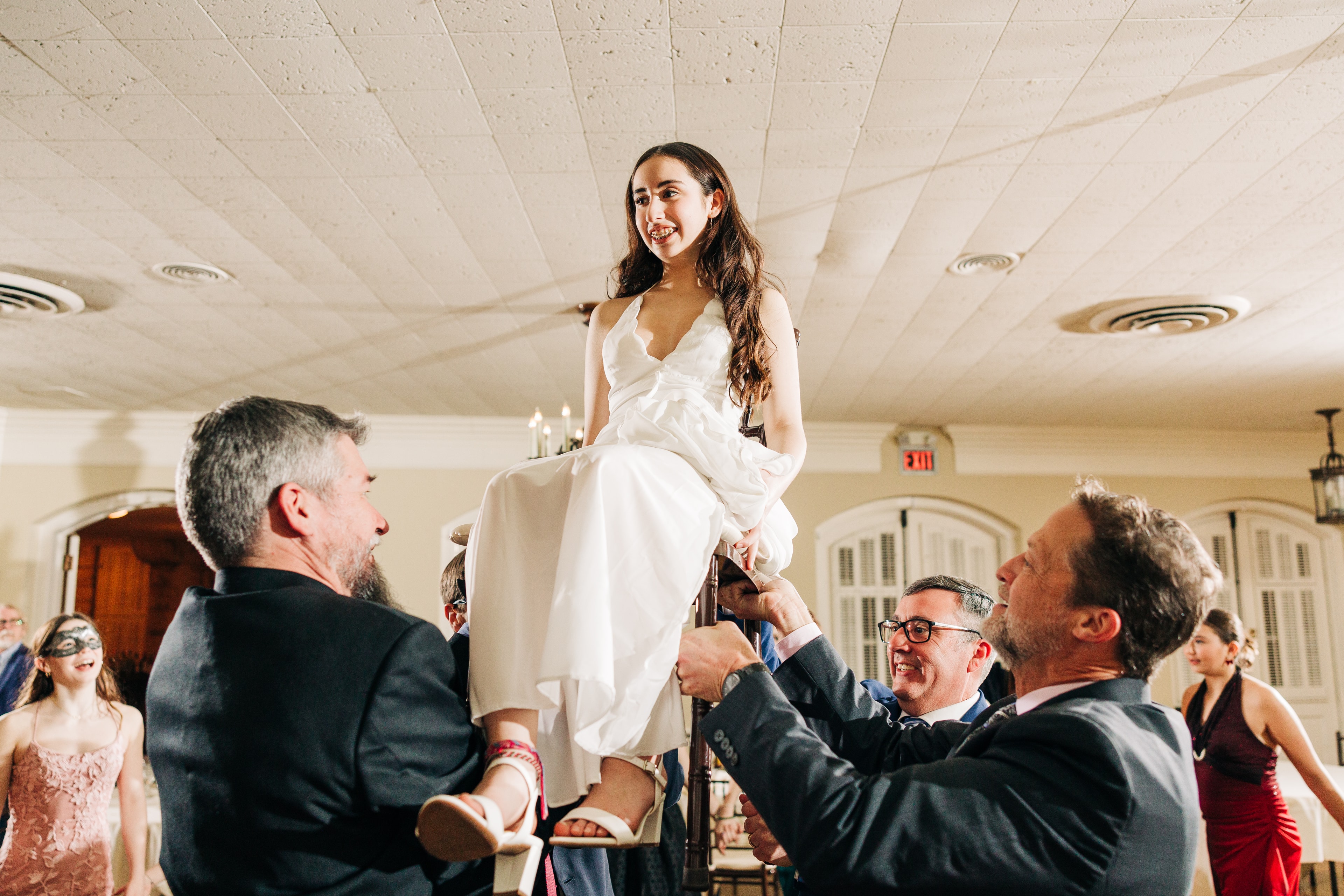 Bat Mitzvah celebration moment — a 13-year-old being lifted in a chair during the hora with friends and family cheering below, or a portrait of the kid looking confident and stylish at their celebration