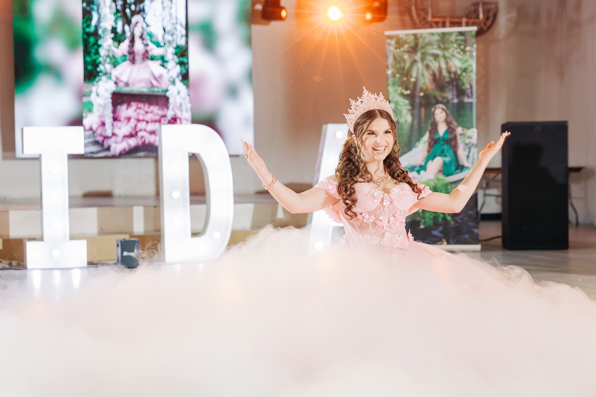 Quinceañera celebration moment — the 15-year old proudly presenting on the dance floor in a soft pink dress as a smoke machine creates an ethereal glow on the dance floor