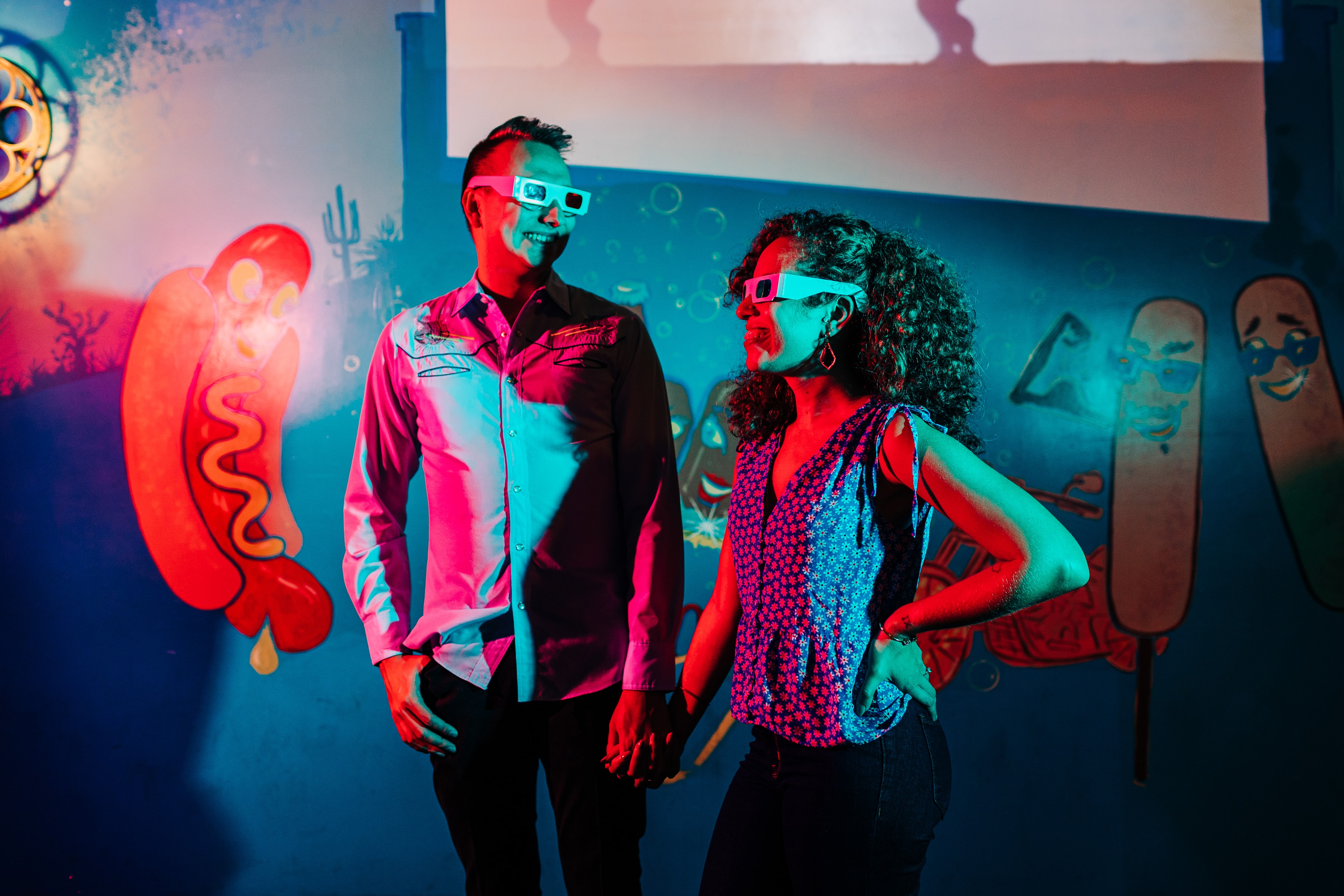 a couple in dramatic red and blue light, wearing 3d glasses inside of a movie theater with dramatic posing
