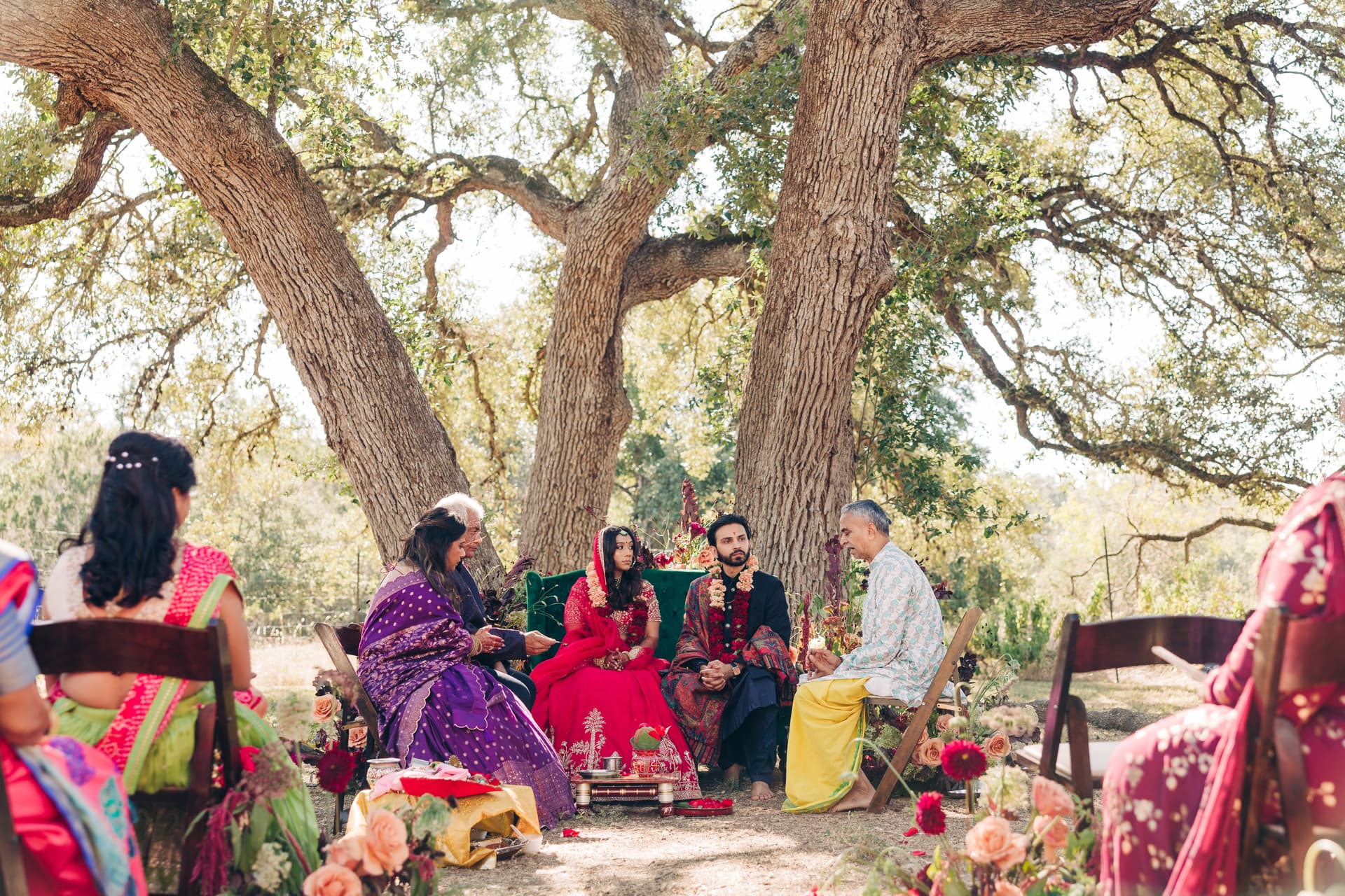 Al fresco ceremony under old oak trees at The Plant at Kyle, surrounded by florals as the couple sits at the couch during their traditional indian wedding ceremony