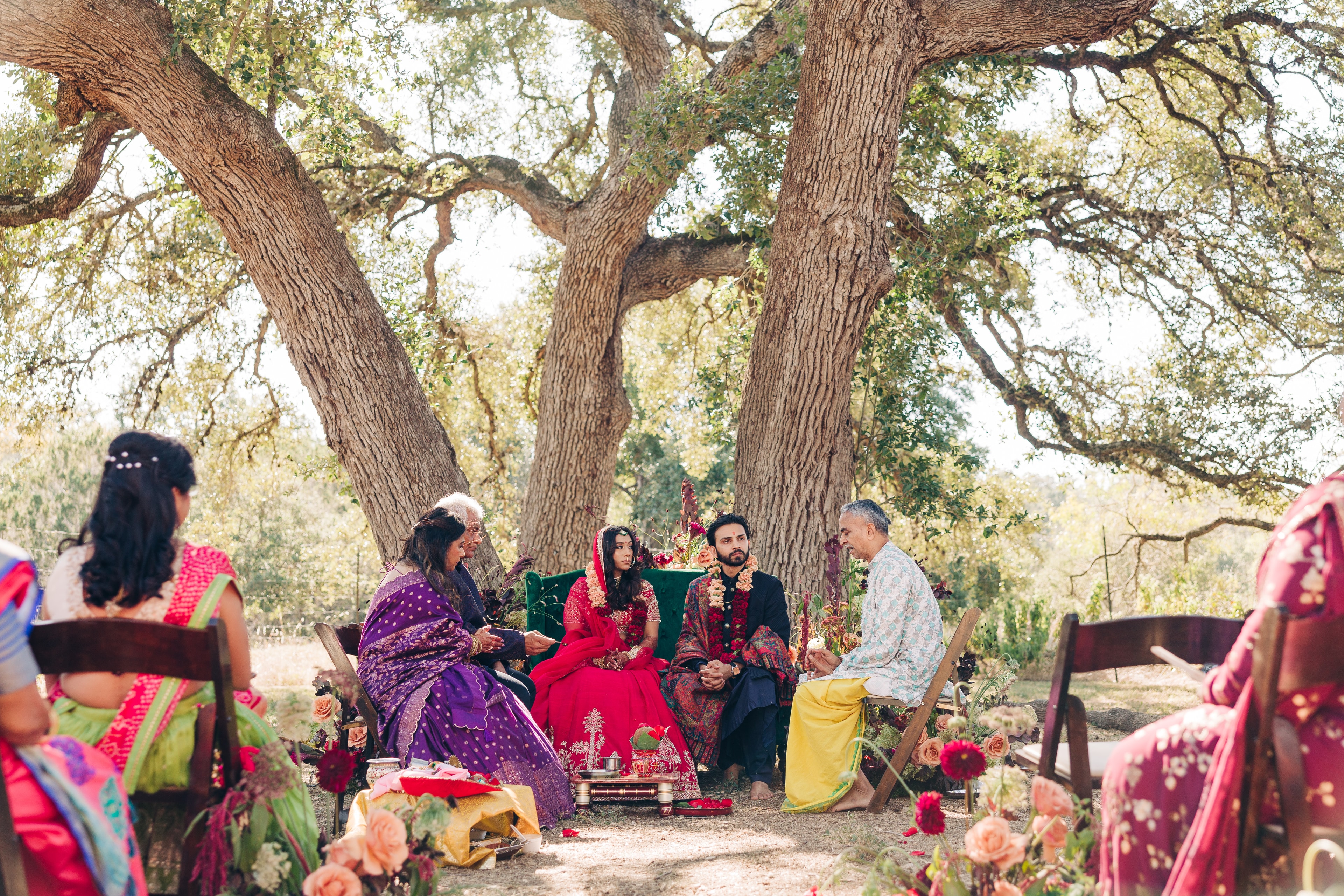 Al fresco ceremony under old oak trees at The Plant at Kyle, surrounded by florals as the couple sits at the couch during their traditional indian wedding ceremony