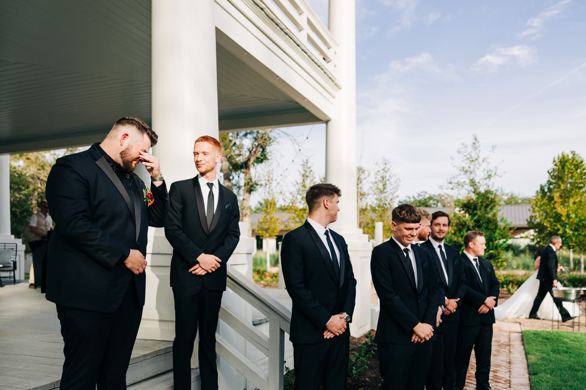 a moment capturing the ceremony walkout, the husband is tearing up as you see his groomsmen emotional in the background, and his wife walking around the corner of the building to emerge down the aisle.